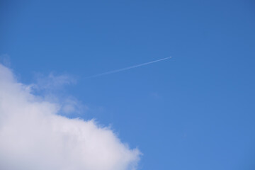 Distant passenger jet plane flying on high altitude on blue sky with white clouds leaving smoke trace of contrail behind. Air traveling concept