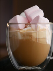 A transparent glass cup of coffee with pink marshmallows