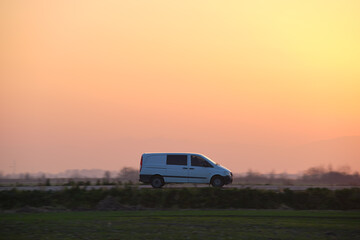 Passenger van driving fast on intercity road at sunset. Highway traffic in evening