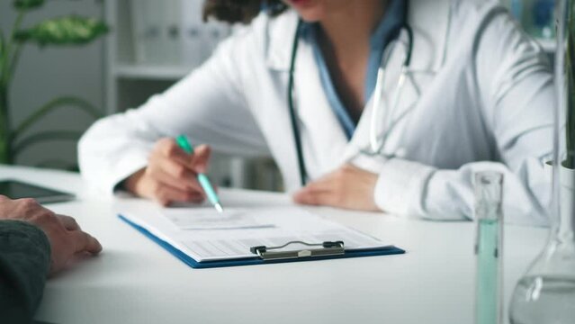 Doctor and patient are sitting at the table. Doctor writes text on paper. The doctor gives the patient a written prescription on paper. Communication between a doctor and a patient treatment for a dis
