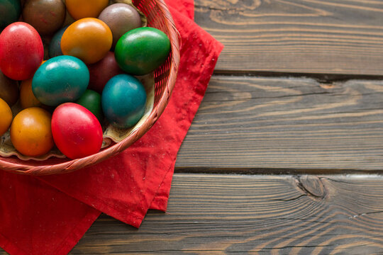 Top view of a Easter colored eggs in a red wicker basket on a table of wooden planks