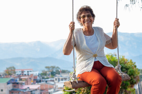 An older woman enjoys her retirement and laughs as she plays in nature and swings on a swing.