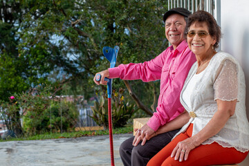 Elderly married couple looking at the camera while smiling. Elderly couple sitting on a wooden bench in the courtyard of their farm in nature.