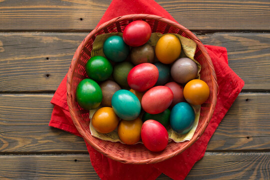 Top view Easter colored eggs in a red wicker basket on a table of wooden planks