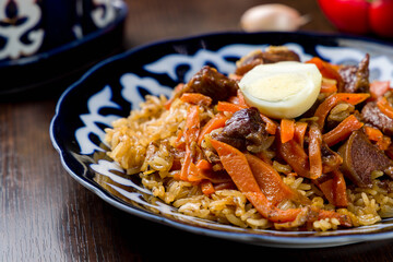 pilaf with beef, carrots and egg on wooden table macro close up