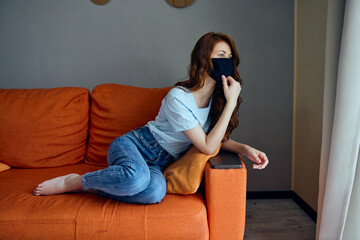 Obraz premium pretty woman in black protective masks sitting on the couch at home Lifestyle