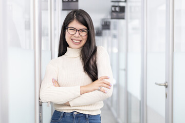 White woman standing on a office corridor smiling with crossed arms