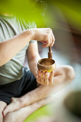 Man using brass gold copper meditation bowl on yoga mat in apartment with candles and plants