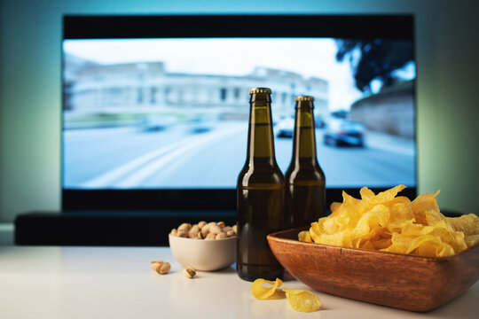 A wooden bowl of chips and snacks in the background the TV works. Evening cozy watching a movie or TV series at home with glass of beer