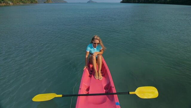 Pretty slim woman in elegant swimsuit lies in pink plastic kayak drifting on azure ocean at exotic resort upper view. Traveling to tropical countries. Girl is sailing on kayak in ocean, view above.