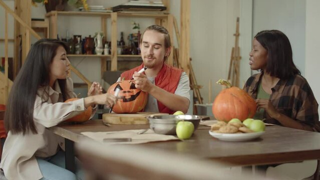 Girls are looking how their friend is painting over a halloween pumpkin's face