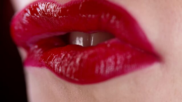 Close-up of sexy woman bites her red lips with desire. Seductive sensual facial expression. Flirt, smile, glossy makeup