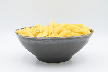 Raw penne rigate pasta, in a dark grey bowl, isolated on a white background
