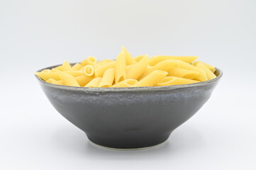 Raw penne rigate pasta, in a dark grey bowl, isolated on a white background
