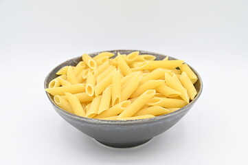 Raw penne rigate pasta, in a dark grey bowl, isolated on a white background
