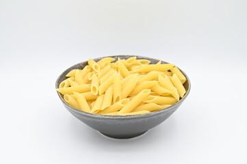Raw penne rigate pasta, in a dark grey bowl, isolated on a white background
