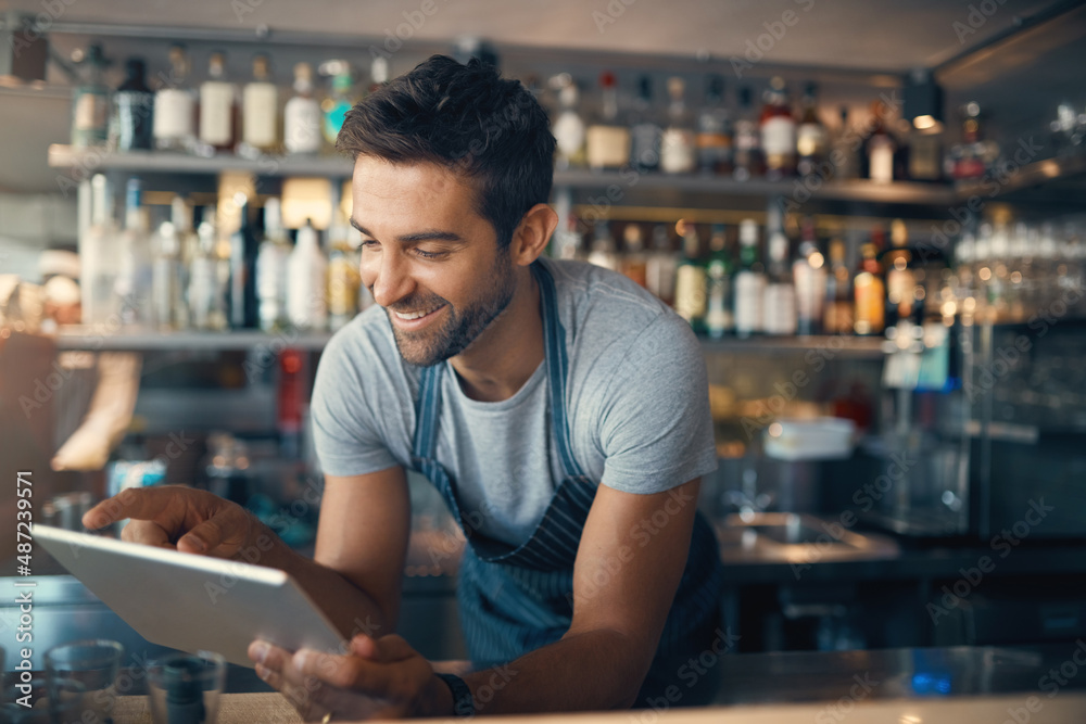 Poster Streamlining small business tasks with smart tech. Shot of a young man using a digital tablet while working behind a bar counter.
