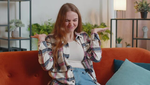 Funny amusing young funny woman in shirt looking awkward making playful silly facial expressions and grimacing, fooling around, showing tongue making stupid brainless dumb expression indoors at home