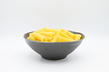 Raw Tortiglioni pasta, in a dark grey bowl, isolated on a white background

