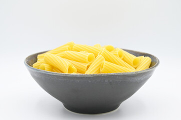 Raw Tortiglioni pasta, in a dark grey bowl, isolated on a white background
