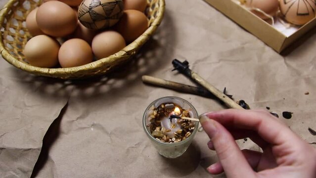 Female hand holding match and burning candle. Preparing for painting Ukrainian Easter eggs decorated with folk designs using a wax resist method. Easter egg. Graphic folk sketch. Wax tool