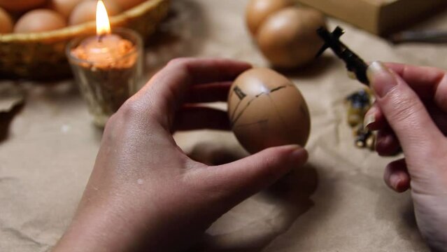 Female hand holding pen, pysachok, and egg and painting it. Preparing for painting Ukrainian Easter eggs decorated with folk designs using a wax resist method. Pysanka, Easter egg. Symbol