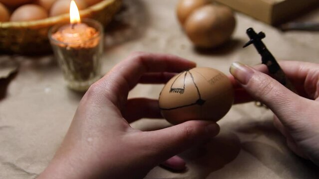 Female hand holding pen, pysachok, and egg and painting it. Preparing for painting Ukrainian Easter eggs decorated with folk designs using a wax resist method. Pysanka, Easter egg
