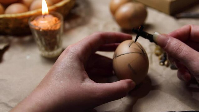 Female hand holding pen, pysachok, and egg and painting it. Preparing for painting Ukrainian Easter eggs decorated with folk designs using a wax resist method. Pysanka, Easter egg. Symbol, pattern
