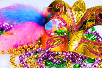 Golden carnival mask and colorful beads on white background. Closeup symbol of Mardi Gras or Fat...