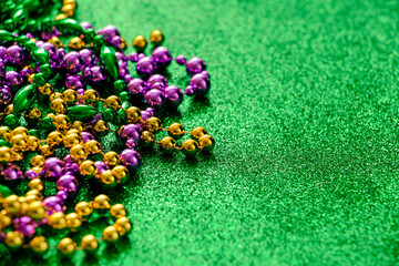 Mardi Gras concept. Multi-colored beads on green shiny background. Fat Tuesday symbol.