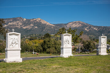 Santa Barbara, California, USA - February 8, 2022: Calvary Cemetery. Landscape with white statues of Station of the Cross 9 to 11 on green burial lawn under blue sky. Santa Ynez mountains.