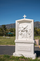 Fototapeta premium Santa Barbara, California, USA - February 8, 2022: Calvary Cemetery. Closeup, white statue of Station of the Cross 8 on green burial lawn under blue sky. Santa Ynez mountains.