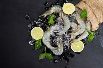 Fresh shrimp with lemon basil leaves on ice Raw shrimp from the sea placed on a black table, seafood menu, top view.