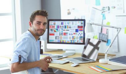 Portrait of young designer sitting at graphic studio in front of laptop and computer while working...