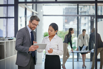 Fototapeta premium This app is going to streamline our internal communication. Shot of a businessman showing something to his female colleague while they stand outside the boardroom.