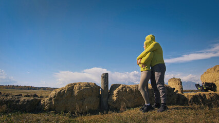 Man and woman in yellow green sportswear. Lovely couple of travelers hug and kiss near old stone...