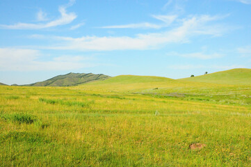 Endless steppes at the foot of high hills overgrown with grass under a summer sunny sky in the clouds.