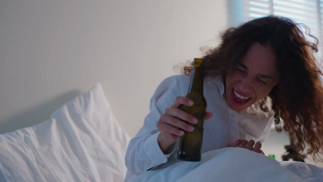 Drunk Latino woman hold beer bottle, feel hangover and dancing on bed.