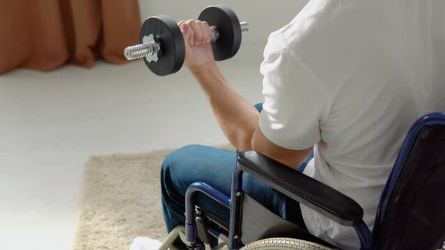 Disabled athlete in wheelchair performs exercises with umbbells, home training and physical activity