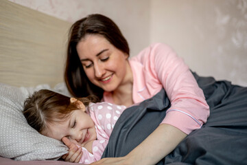 Beautiful mother in pajamas sleeping in bed and hugging little daughter. Happy family. Leisurely morning.