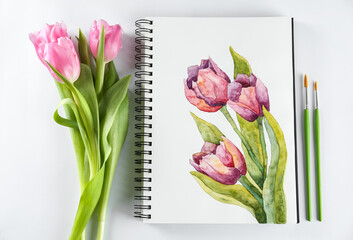 Painting of tulips in sketchbook, flowers and brushes on white background, flat lay