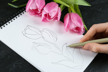 Woman sketching tulips in notebook at black table, closeup