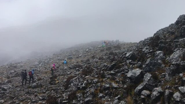 Five hikers are ascending a trail of volcanic rocks on the slopes of Sincholagua, a dormant volcano of Ecuador. Mist is present.