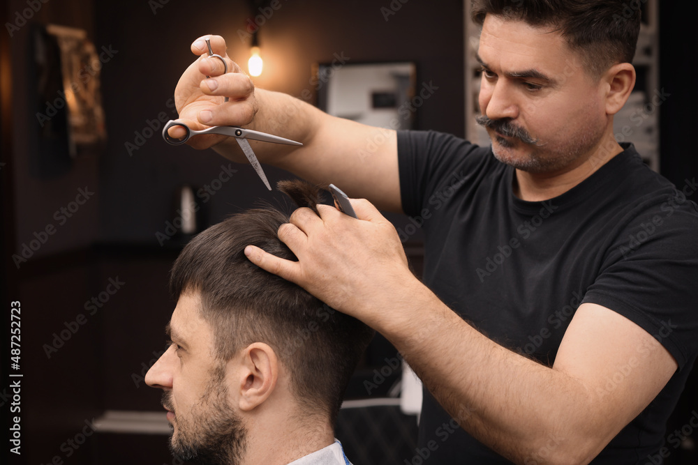 Wall mural Professional hairdresser cutting man's hair in barbershop