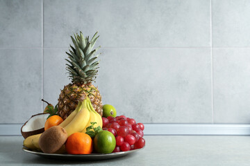 Plate with different ripe fruits on grey table. Space for text