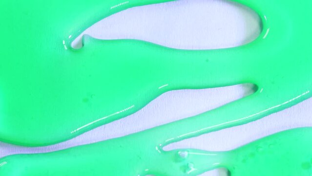 Green translucid dense substance falling in white surface background. Jelly, slime artistic drawing. Sticky product drops and spreads in paper. Colour contrast macro shot, close up.