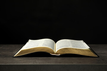 Open Bible on grey table against black background