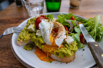 Sourdough toast, poached eggs, avocado pulp and fresh vegetables on plate in cafe, close up
