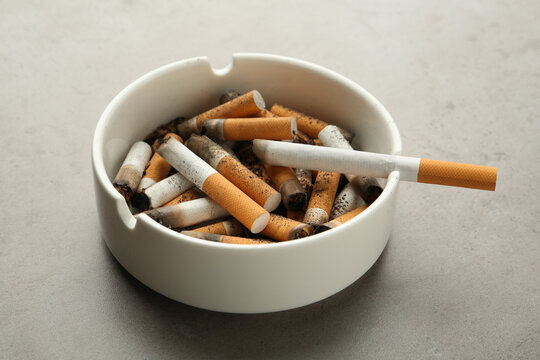 Ceramic ashtray full of cigarette stubs on grey table