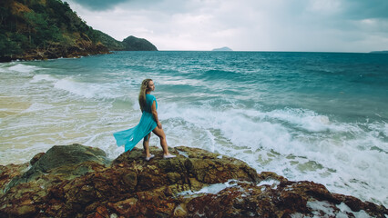 Fototapeta na wymiar Sexy hot woman meditates, relaxes on a rock reef hill in stormy morning rain cloudy sea. Girl in blue swimsuit, dress tunic. Concept feminine, relax, sexual health. Dark dramatic silhouette view